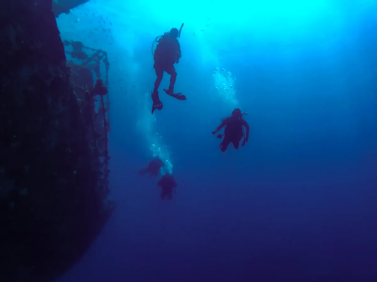 A group of scuba divers exploring a submerged shipwreck in the deep blue waters of Saudi Arabia.