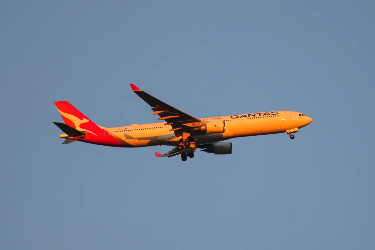 A vibrant Qantas passenger plane in flight against a clear blue sky during sunset.